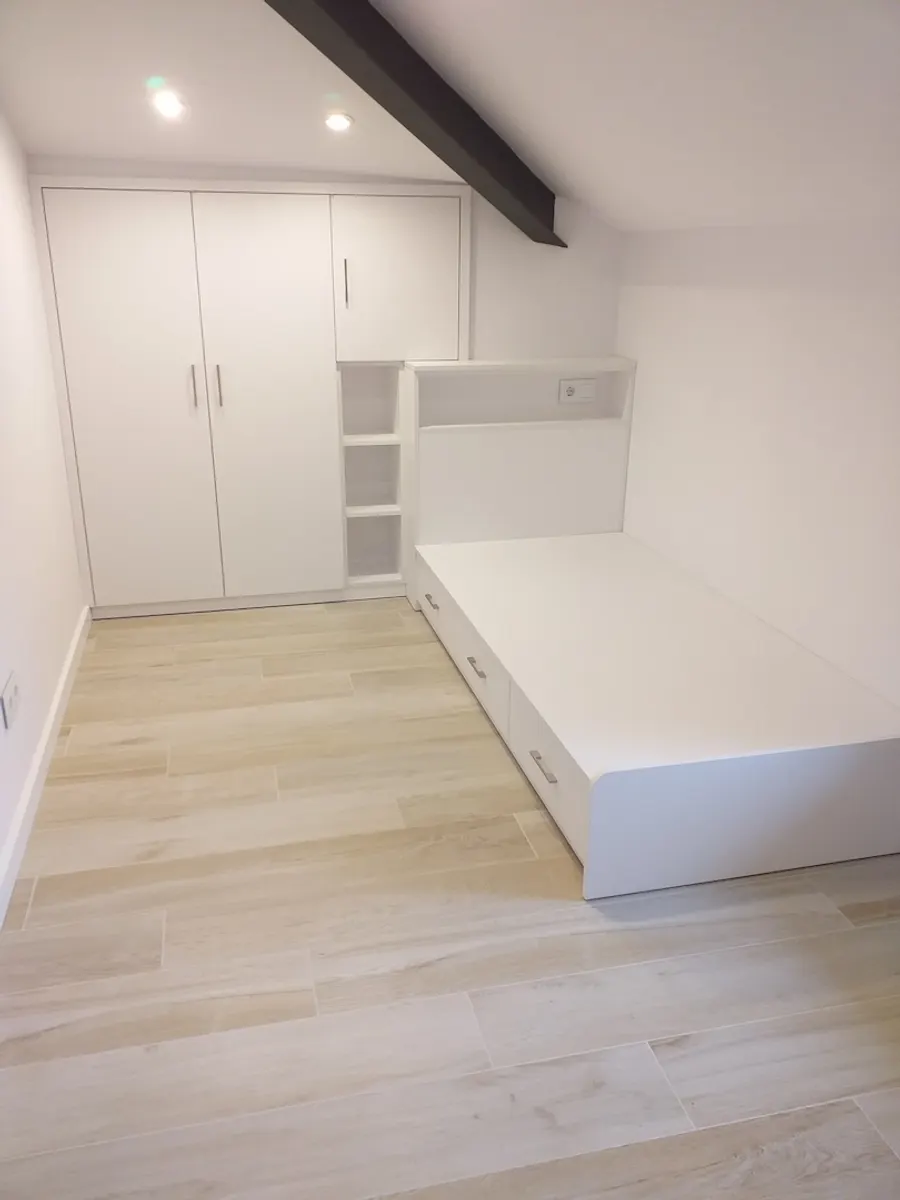 Armari blanc a mida al costat d'un llit amb calaixos