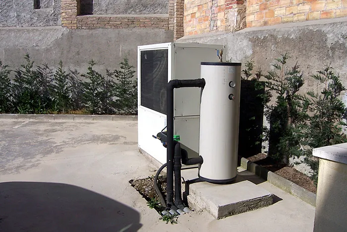 Bomba de calor amb dipòsit acumulador al pati d'una casa